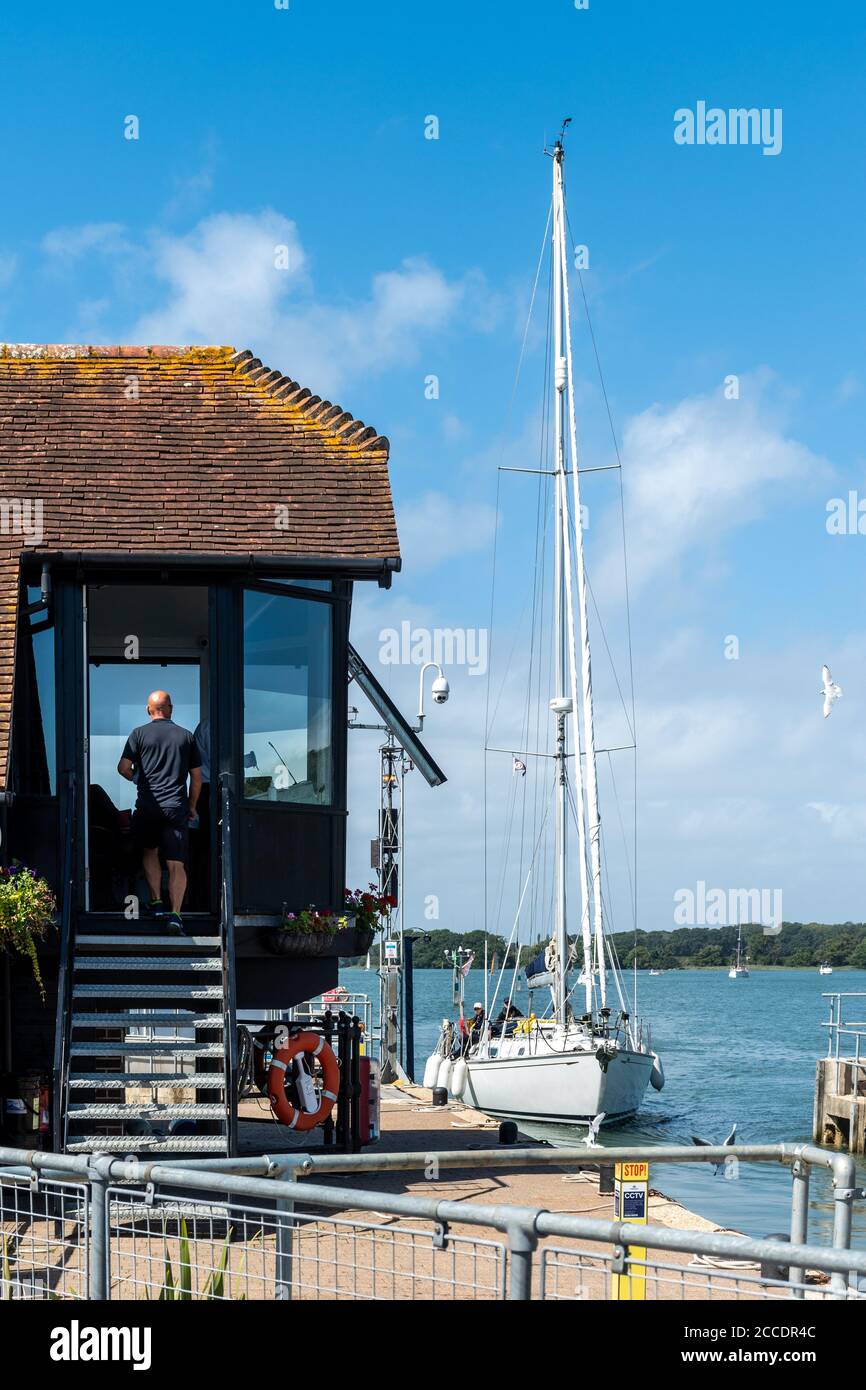 Entrance to Chichester Marina via the lock, Chichester Harbour, West Sussex, UK - a yacht sailing into the marina past the lock control building Stock Photo