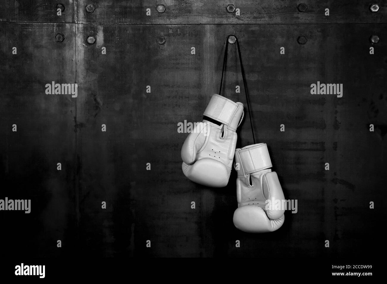 Close up pair of white leather boxing gloves hanging over black wall