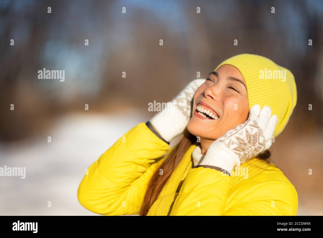 Happy winter woman enjoying cold with yellow hat protecting ears, gloves, coat for frost protection. Asian girl smiling. Stock Photo