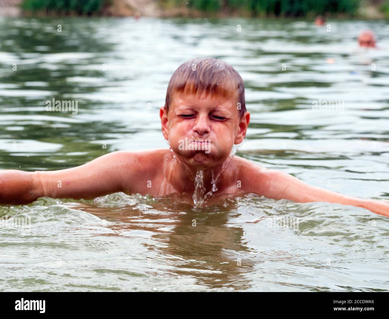 Water runs down the face of a Caucasian boy emerging from the lake Stock Photo
