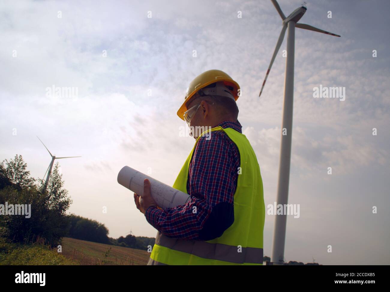 Engineer in a wind turbine. A man in a helmet supervises the operation of the electric windmills. Ecology and renewable energy sources concept. Stock Photo