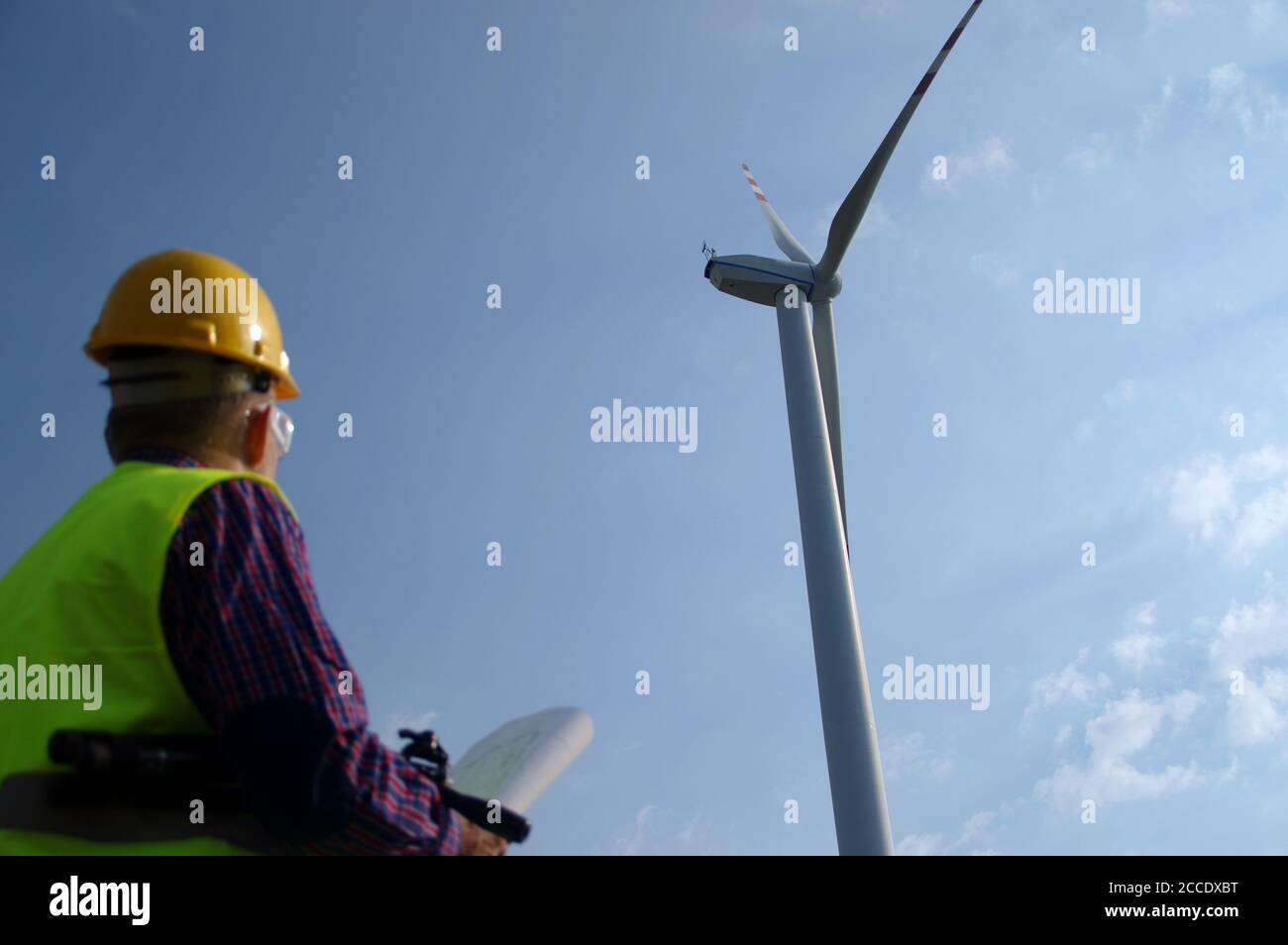 Engineer in a wind turbine. A man in a helmet supervises the operation of the electric windmills. Ecology and renewable energy sources concept. Stock Photo
