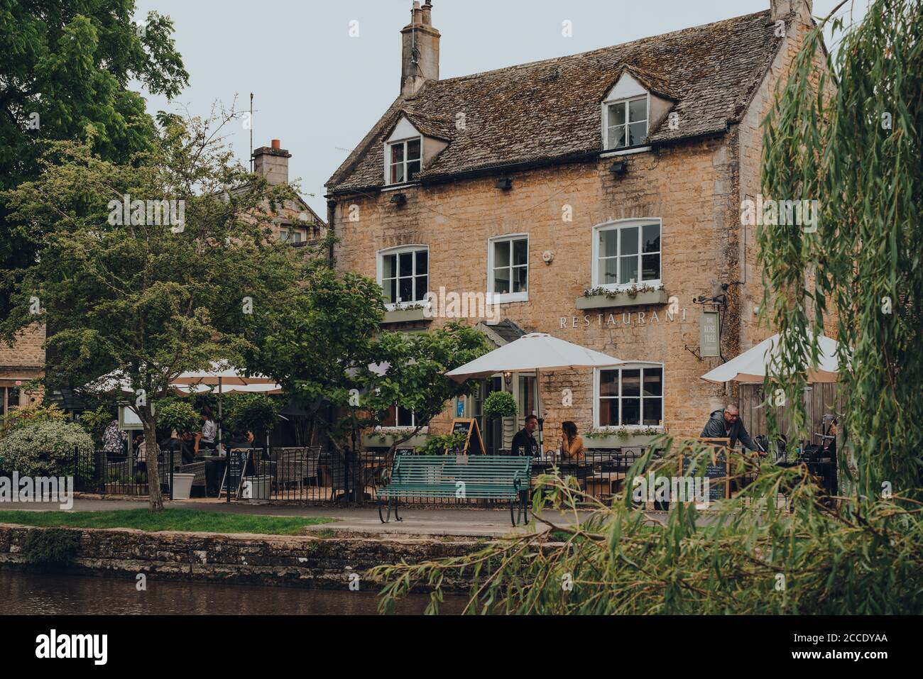 Bourton-on-the-Water, UK - July 12 2020: People at the outdoor tables of The Rose Tree Restaurant by River Windrush in Bourton-on-the-Water, a famous Stock Photo