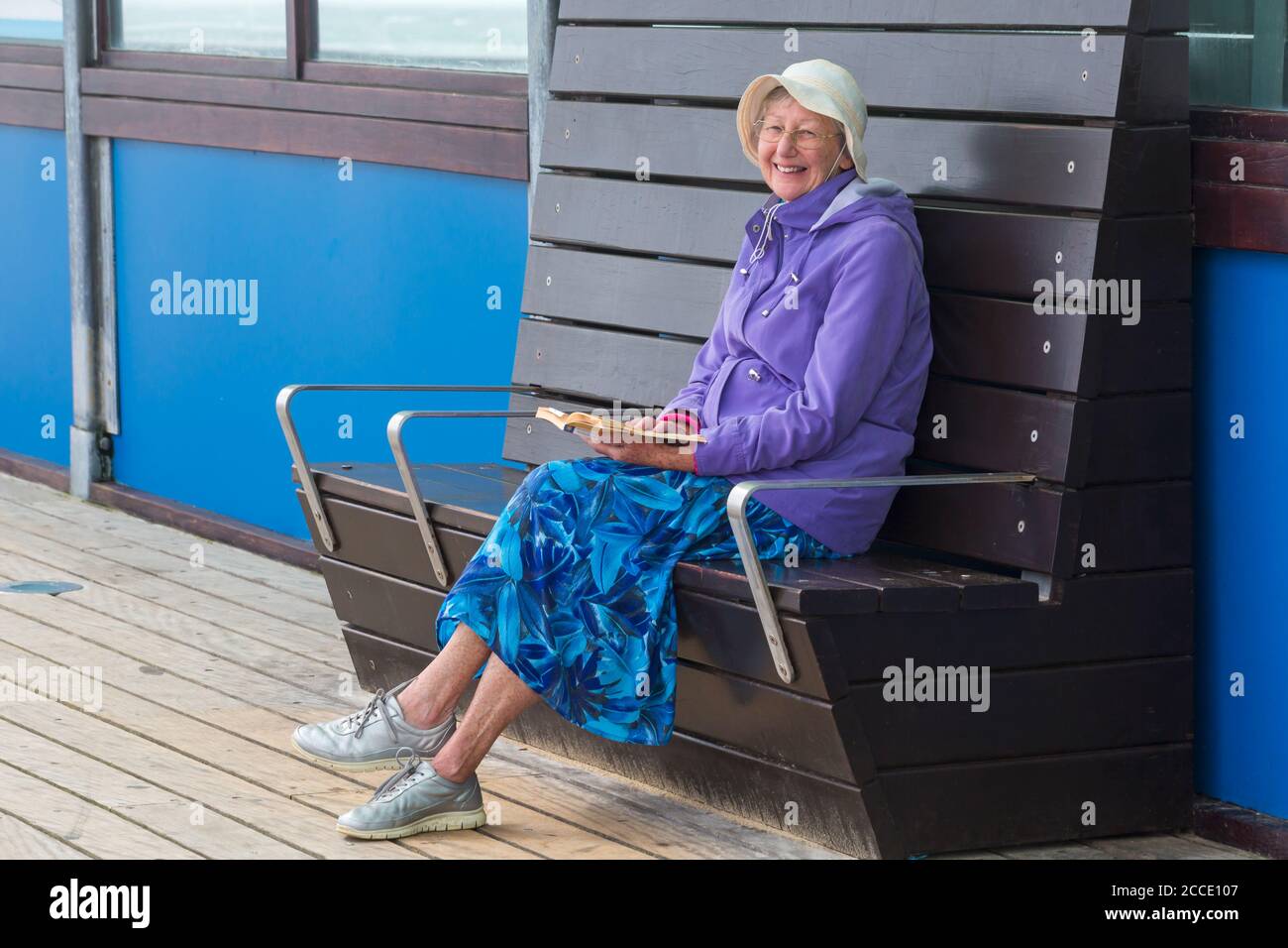 Storm Ellen brings strong wind and rough seas at Bournemouth beach, Dorset UK in August - senior lady sitting on pier reading book sheltered from wind Stock Photo
