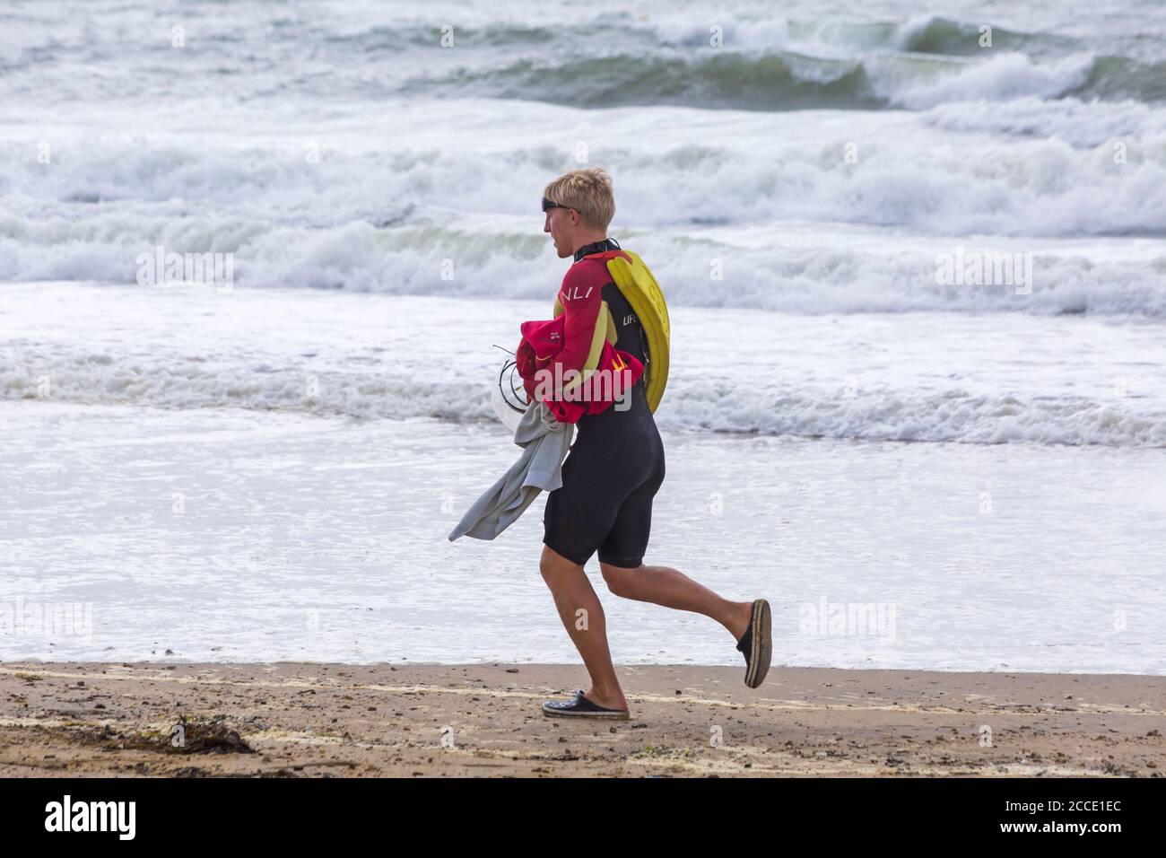 Storm Ellen brings strong wind and rough seas at Bournemouth beach, Dorset UK in August - RNLI lifeguard walking along seashore Stock Photo
