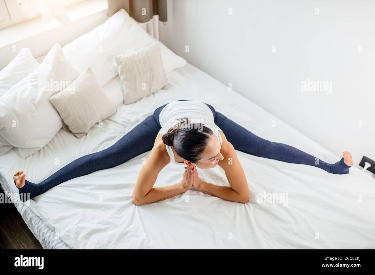caucasian fitness woman stretching legs and whole body in the morning, sit on bed with legs in different directions Stock Photo