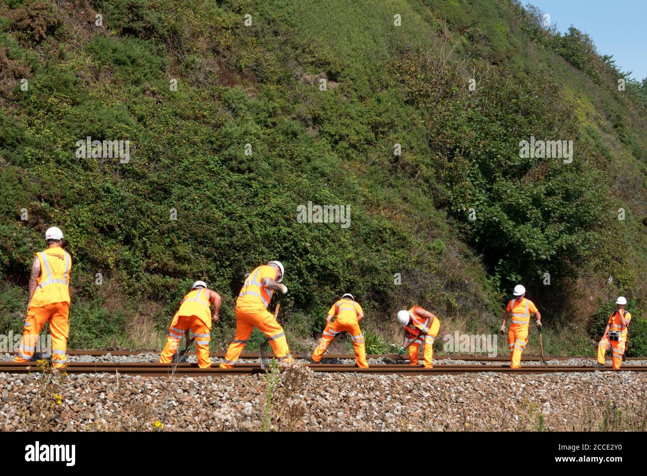 A group, or gang, or Netwok Rail workers carrying out maintenance work on a live railway track. The men are clearing debris from the track using rakes Stock Photo
