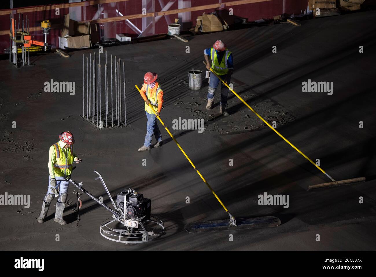 Austin, TX USA July 25, 2020: Concrete workers use long-handled screeds and power trowels to level and smooth concrete on the parking garage floor of a 53-story building during a night-time pour in downtown Austin, TX. Huge construction projects continue unabated in Texas despite the nationwide COVID-19 pandemic and the state stricken with over a half million cases and 10,000-plus deaths. Stock Photo