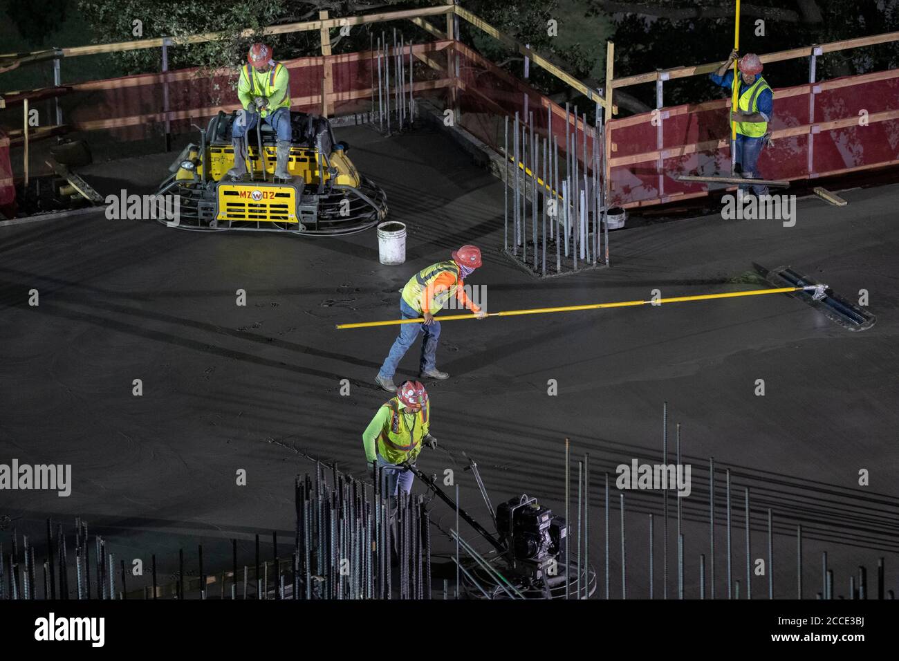 Austin, TX USA July 25, 2020: Concrete workers use long-handled screeds and power trowels to level and smooth concrete on the parking garage floor of a 53-story building during a night-time pour in downtown Austin, TX. Huge construction projects continue unabated in Texas despite the nationwide COVID-19 pandemic and the state stricken with over a half million cases and 10,000-plus deaths. Stock Photo