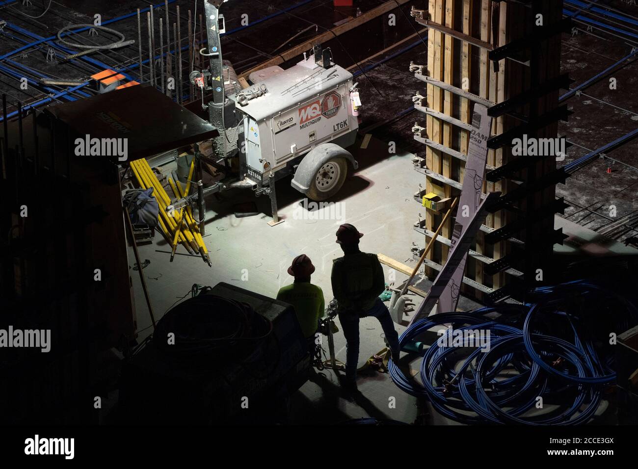 Austin, TX USA July 25, 2020: A generator-powered spotlight shines on concrete crews working on the parking garage of a 53-story building during a night-time pour in downtown Austin, TX. Huge construction projects continue unabated in Texas despite the nationwide COVID-19 pandemic and the state stricken with over a half million cases and 10,000-plus deaths. Stock Photo