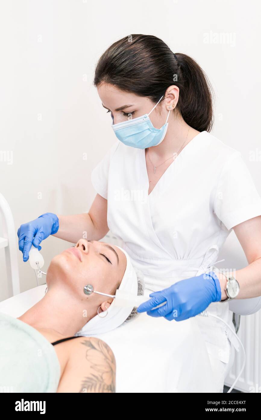 The young female client of cosmetic salon having microcurrent procedure on her face with special devices, close-up. Beautician using electrical impuls Stock Photo