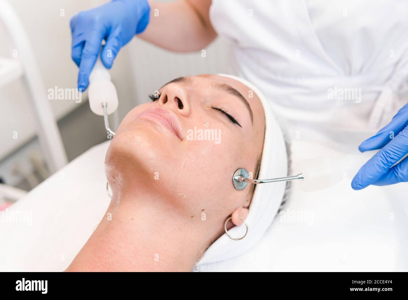 The young female client of cosmetic salon having microcurrent procedure on her face with special devices, close-up. Beautician using electrical impuls Stock Photo