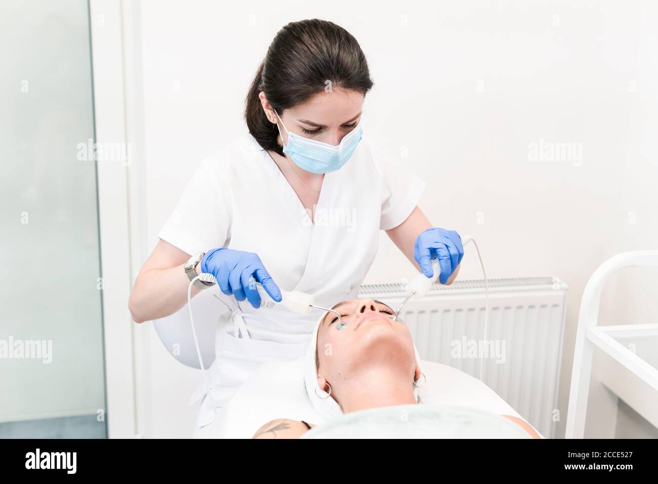 The young female client of cosmetic salon having microcurrent procedure on her face with special devices, close-up. Beautician using electrical impuls Stock Photo
