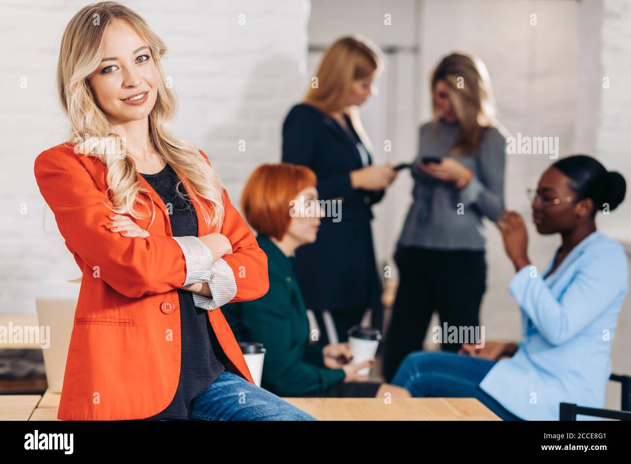 Indoor shot of pleasant-looking female copywriter with long blonde hair, dressed in red coat, being glad to finish her successful project work, looks Stock Photo