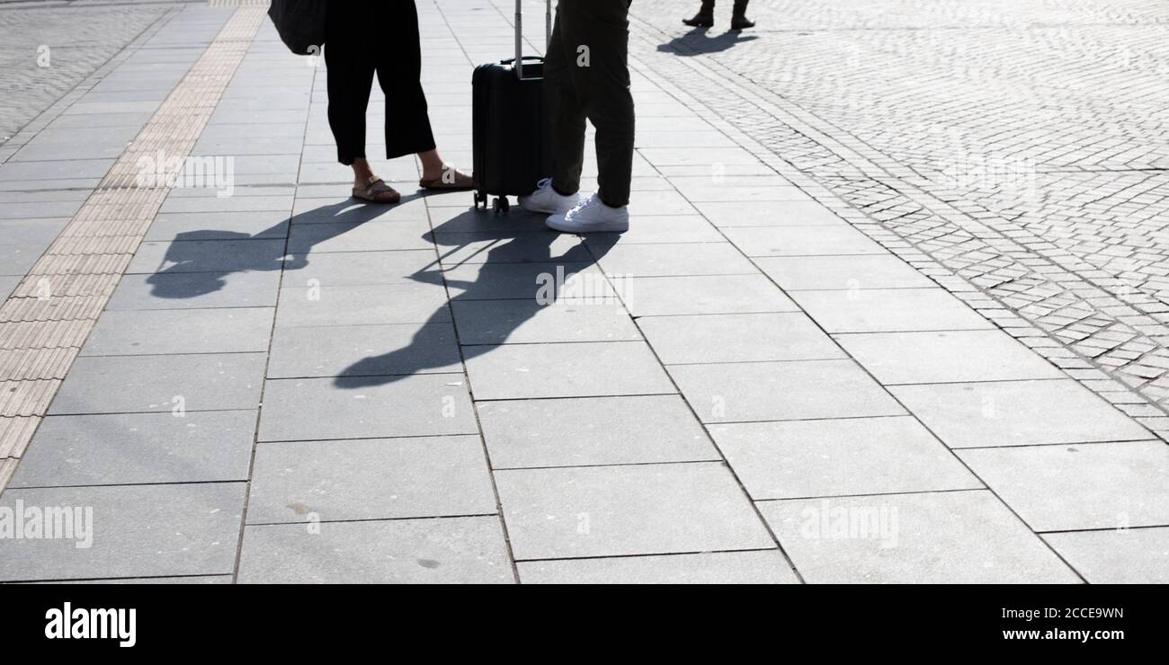 closeup of young couple waiting at the main station with a suitcase between their legs and shadows on the pavement in the foreground Stock Photo