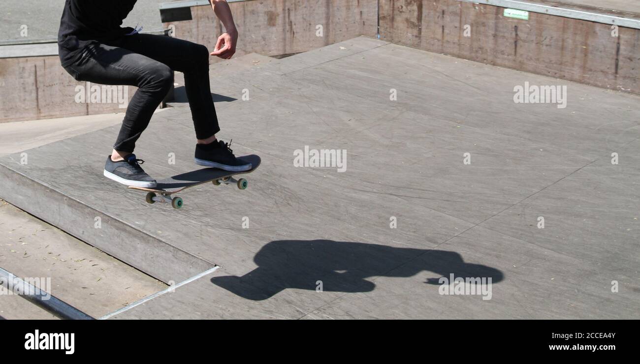 legs of a male youth performing a trick on his skateboard in a skatepark with complete shadow on the ground, action but no person recognizable Stock Photo