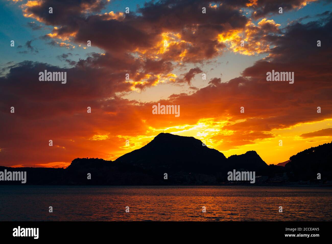 Bright fiery sunset behind the silhouette of a mountain over the sea ...