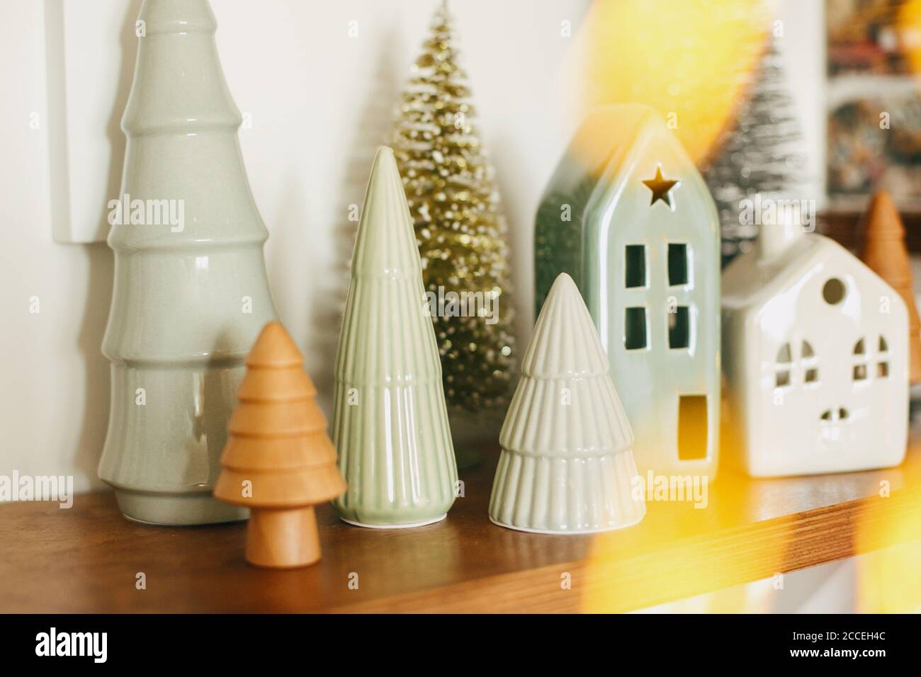 Merry Christmas and Happy Holidays. Modern little christmas ceramic house  and glitter trees on wooden shelf, stylish festive decor. Christmas  miniatur Stock Photo - Alamy