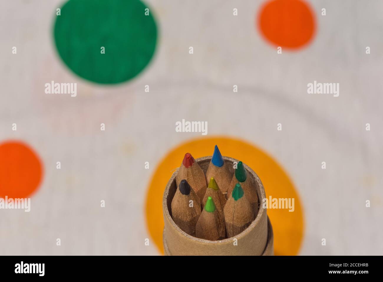 Colored pencils inserted in a cardboard cylinder on a colored plane