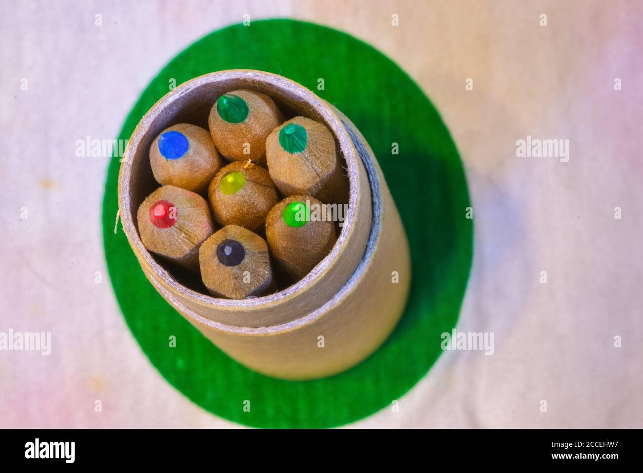 Colored pencils inserted in a cardboard cylinder on a colored plane