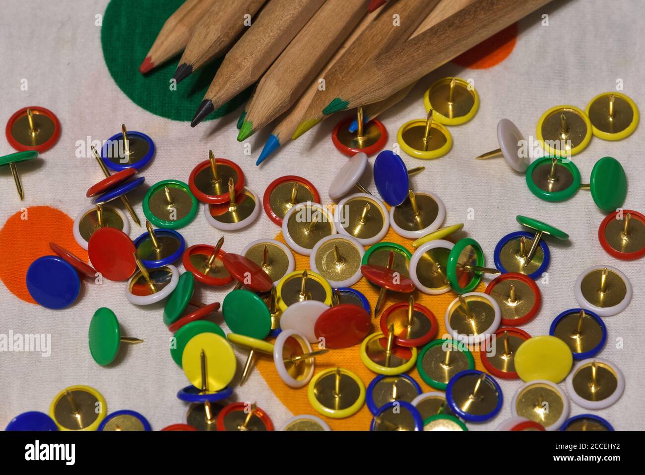 Thumbtacks and colored pencils scattered on a colored plane, horizontal image Stock Photo