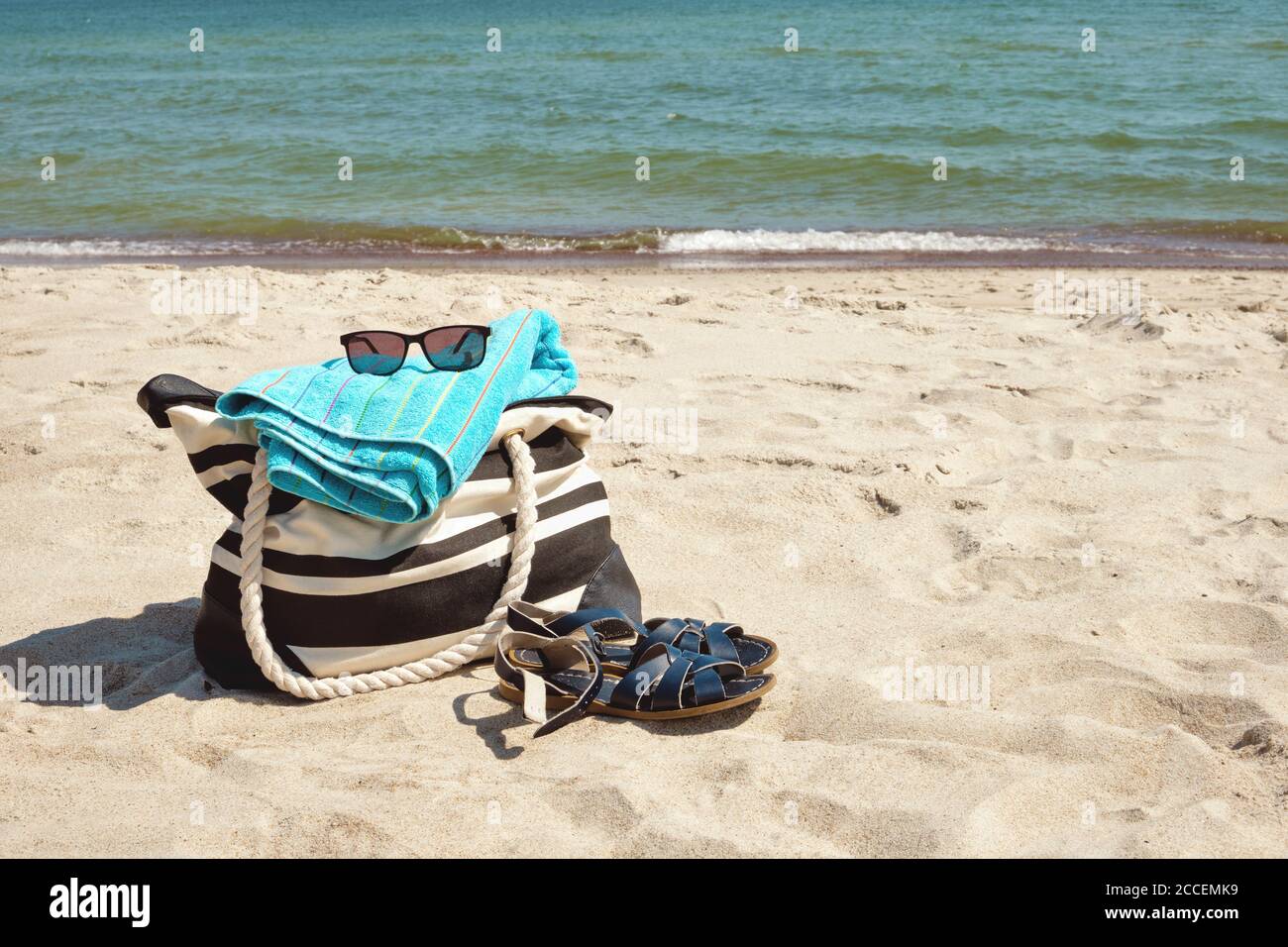 Set of personal belongings lying on the beach sand with calm sea in