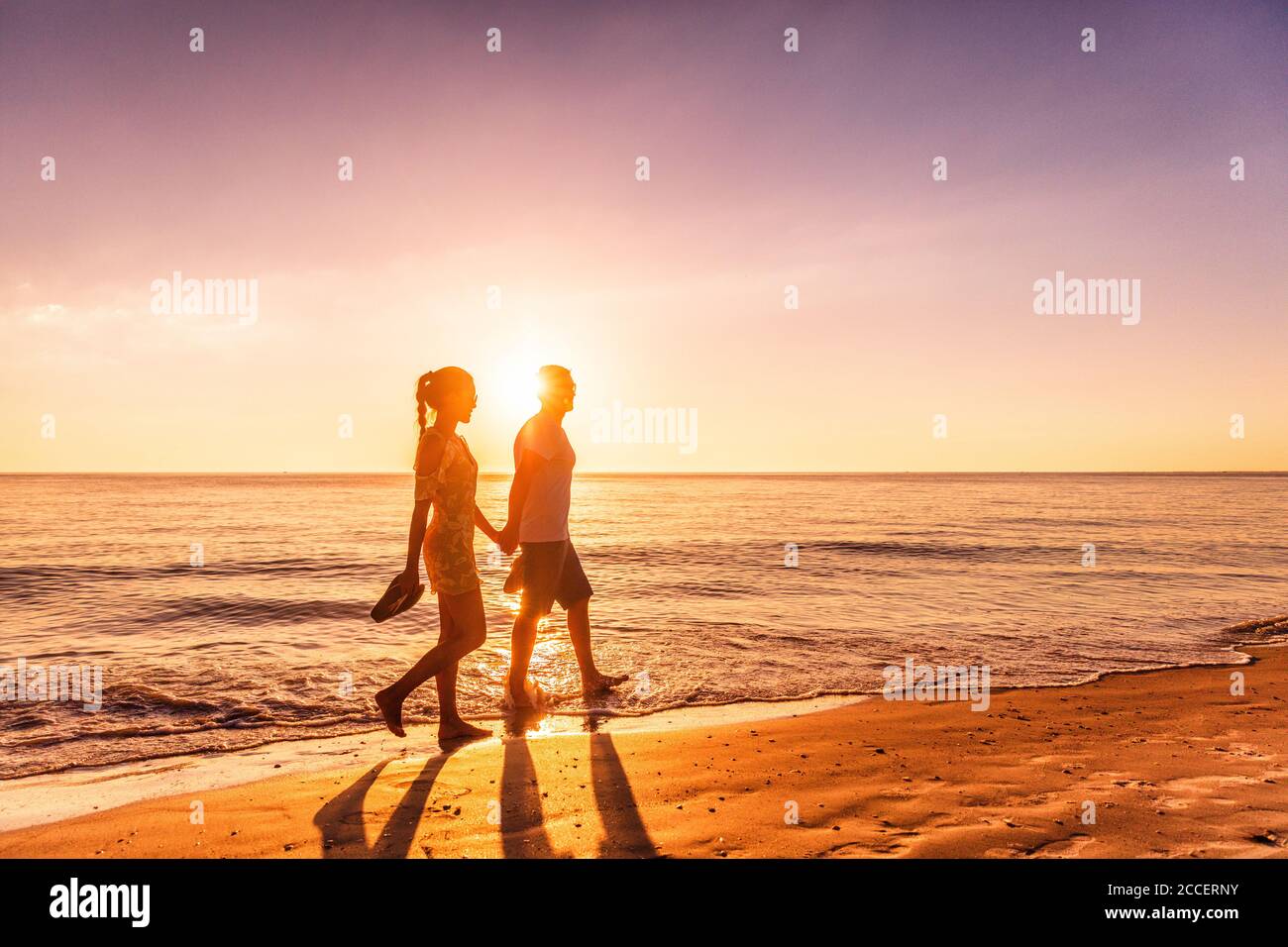 Couple walking on beach at sunset silhouettes - Romantic summer travel holidays in Caribbean destination Stock Photo