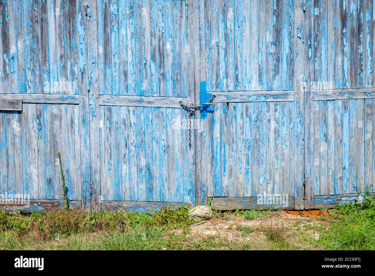 Weathered garage door with peeling blue paint locked with chain hires