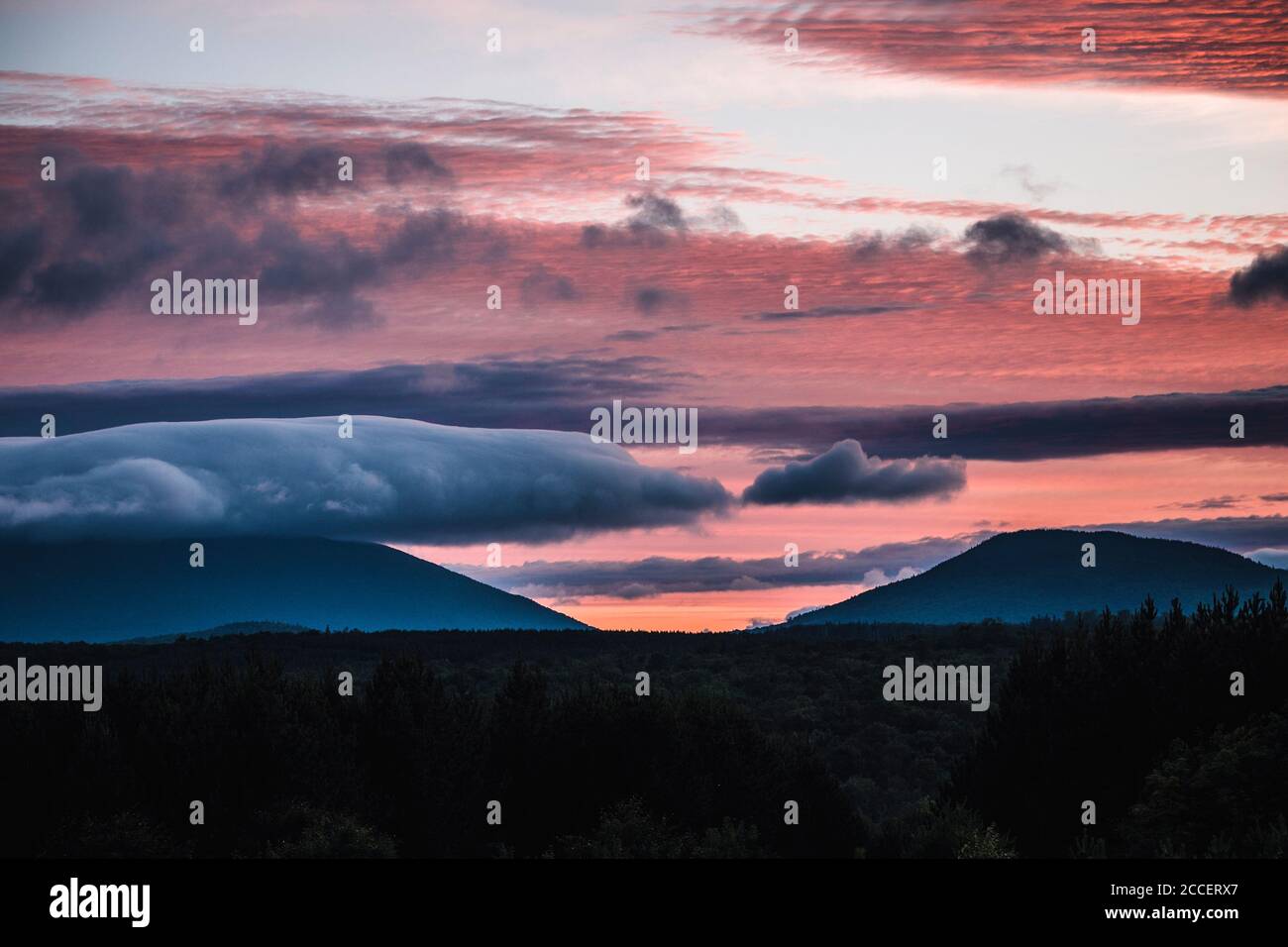 Vibrant red and pink sunset and clouds over distant mountains in Maine Stock Photo