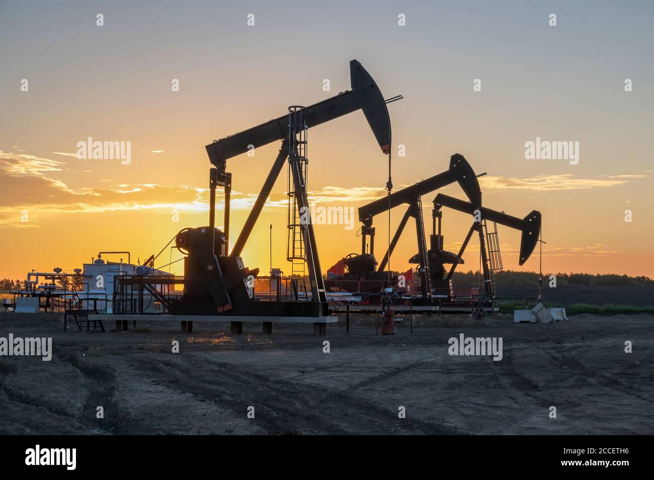 Three oil well pumpjacks at sunrise near Crossfield, Alberta, Canada