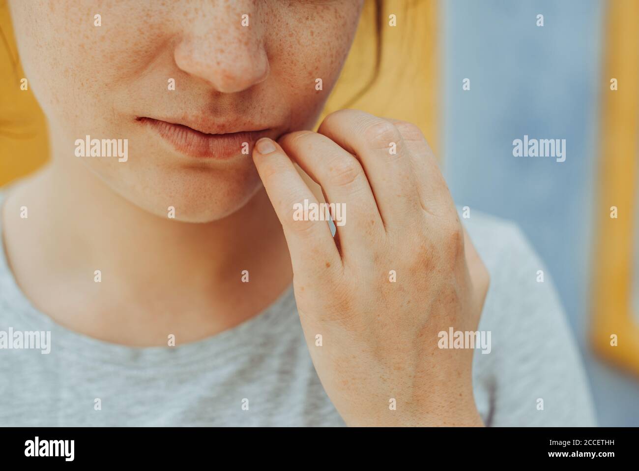 Close up portrait of young woman with freckles holding hand at lips Stock Photo
