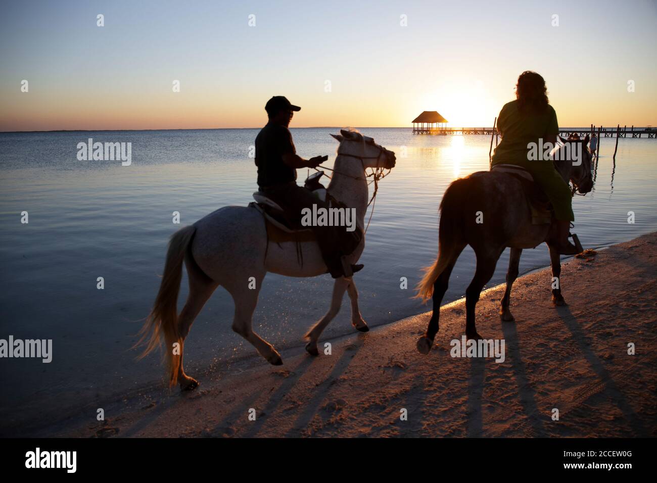 Tourist riding a horse by an idyllic beach of Holbox Island at sunset. Yucatan, Mexico Stock Photo