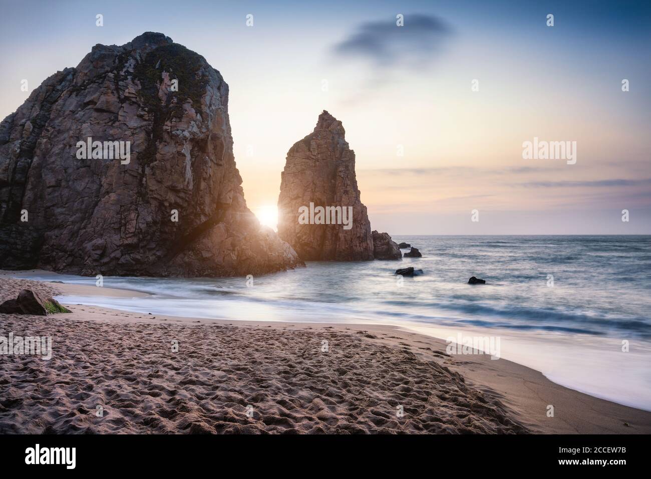 Sunset at Ursa Beach Sea stack, Portugal. Atlantic Ocean Foamy waves rolling to sandy beach. Holiday vacation landscape scene. Stock Photo