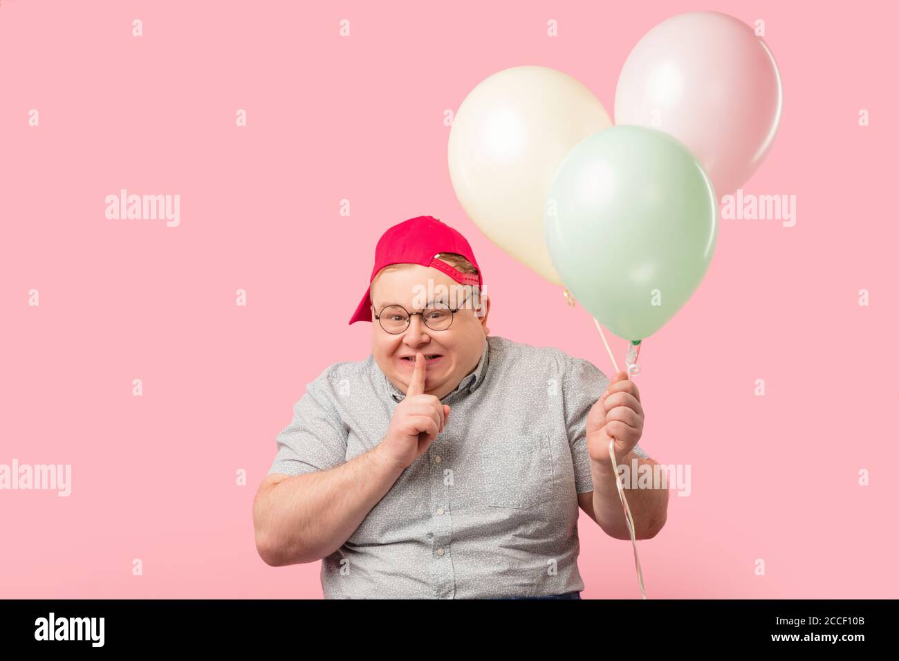 Plump softie man much similar to Winnie the Pooh asks to keep secret that he has air baloons on the birthday of his daughter, keeps finger near his li Stock Photo