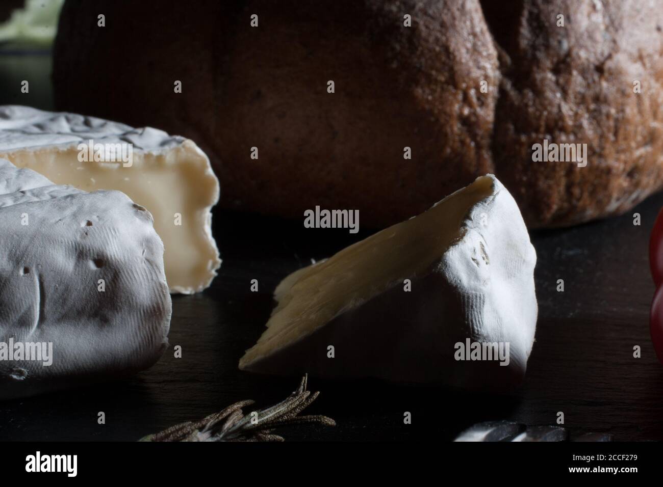 Close up of Fresh French Brie cheese and a one slice on a black stone plate with bread Stock Photo