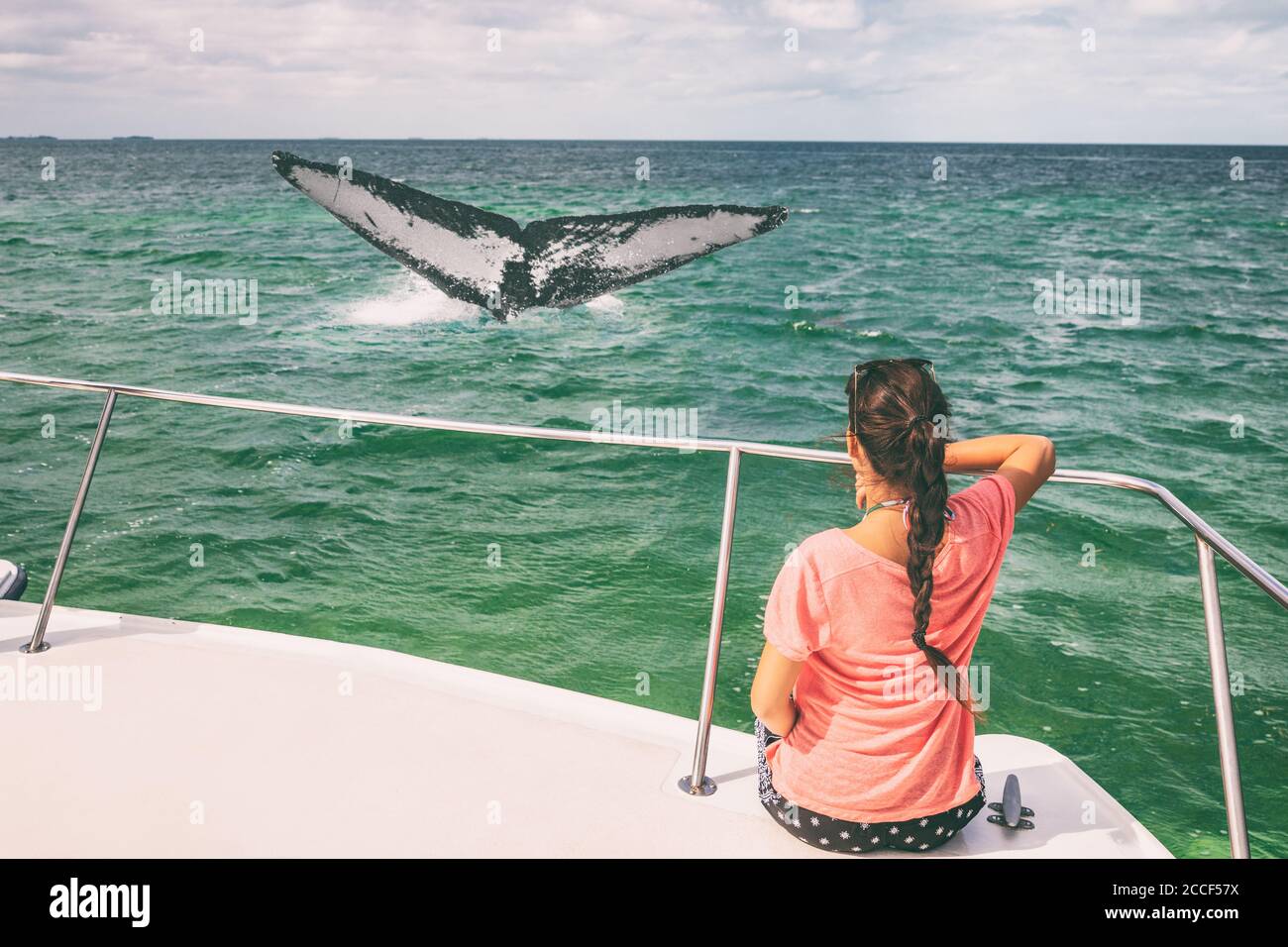 Whale watching boat tour tourist woman relaxing looking at humpback breaching flapping tail travel destination, summer vacation on deck of catamaran Stock Photo
