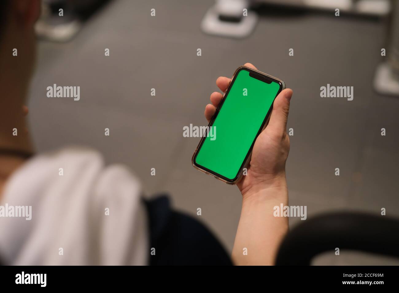 over shoulder of man holding green screen smart phone in the gym. blur background Stock Photo