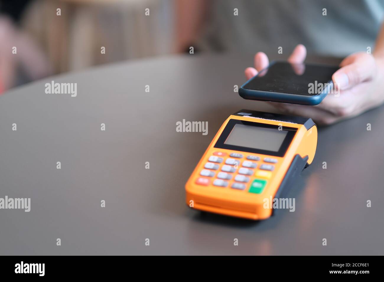 close up hand holding smartphone over pos terminal on table. blur background Stock Photo