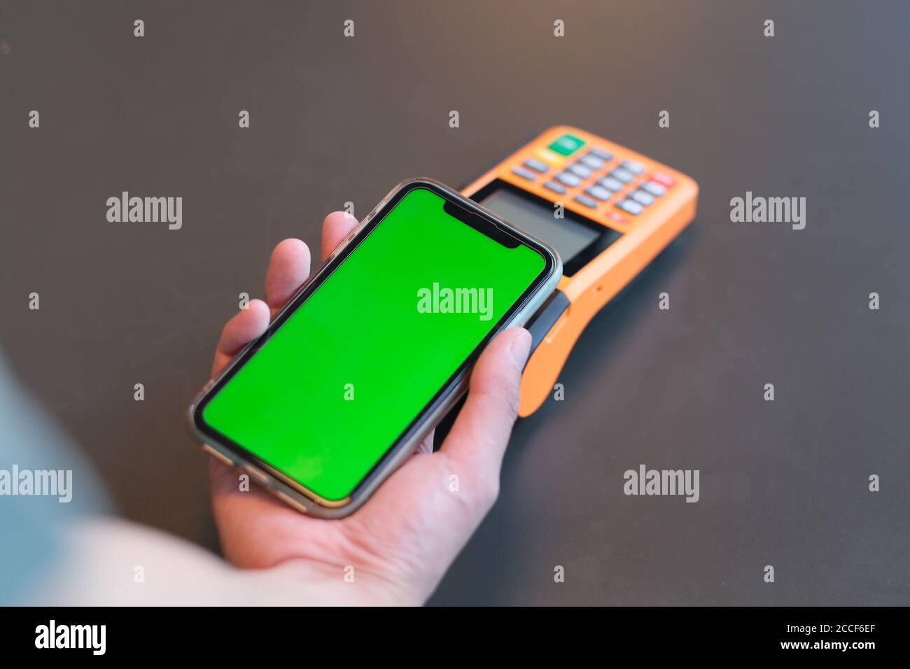 over shoulder view of man holding green screen smart phone over pos terminal on counter. blur background Stock Photo