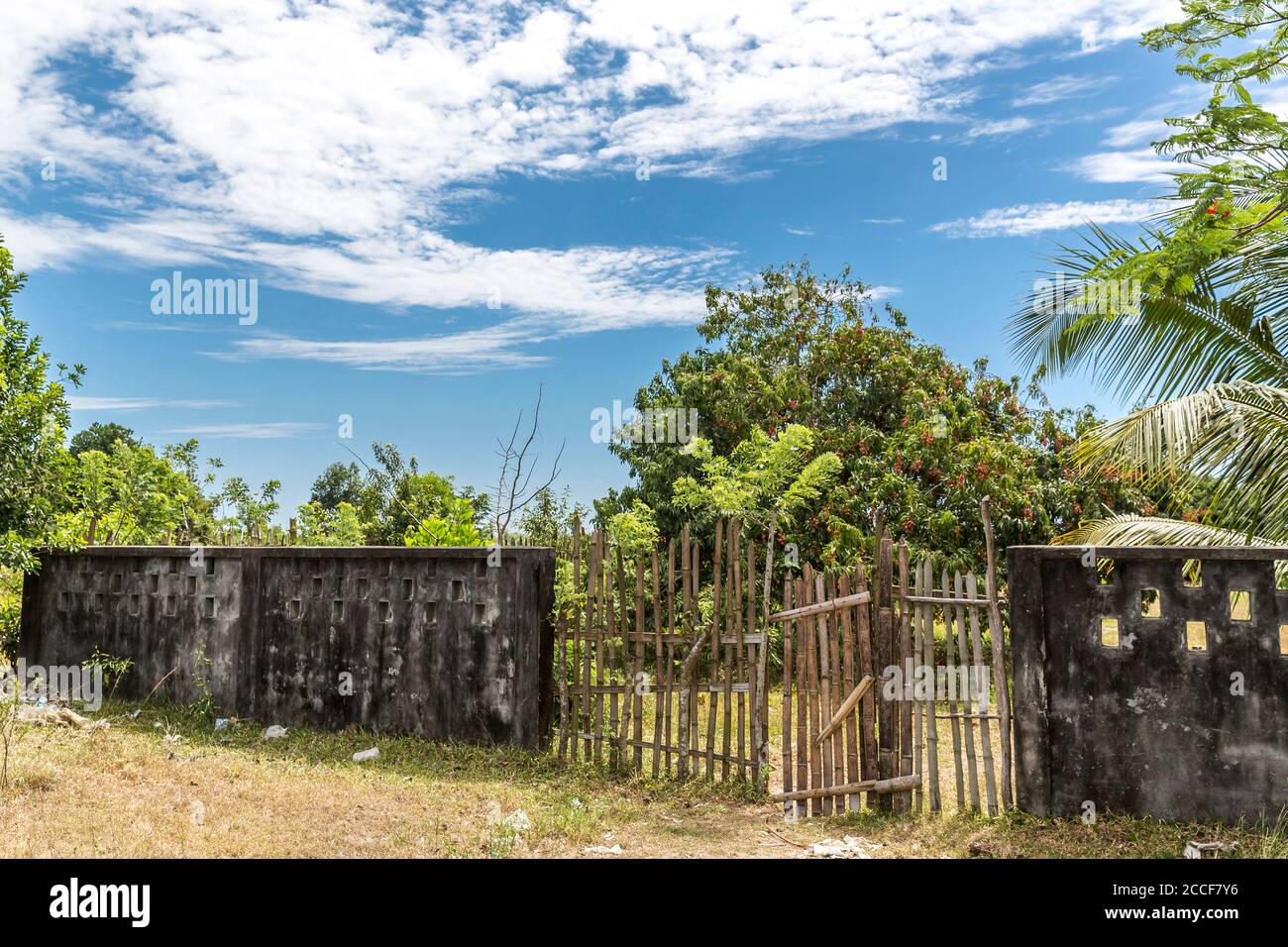 Dilapidated stone wall and gate made of bamboo, behind Litchi tree, Toamasina, Tamatave, Madagascar, Africa, Indian Ocean Stock Photo