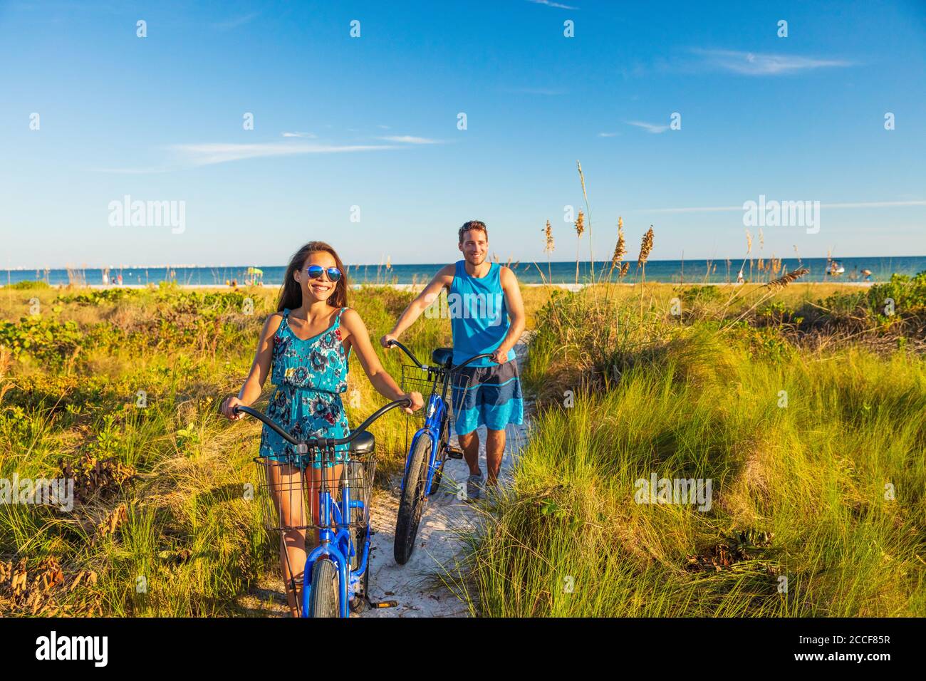 Summer people lifestyle happy couple biking on beach relaxing outdoors activity at sunset. Young woman and man riding recreational bikes bicycles on Stock Photo