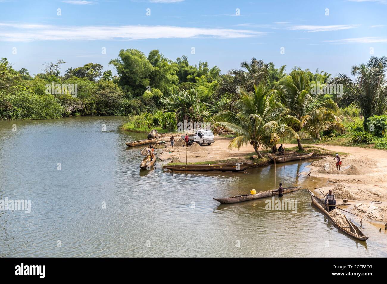 Local men and women unload sand from dugout canoes, Ivoloina River, Taomasina, Tamatave, Madagascar, Africa, Indian Ocean Stock Photo
