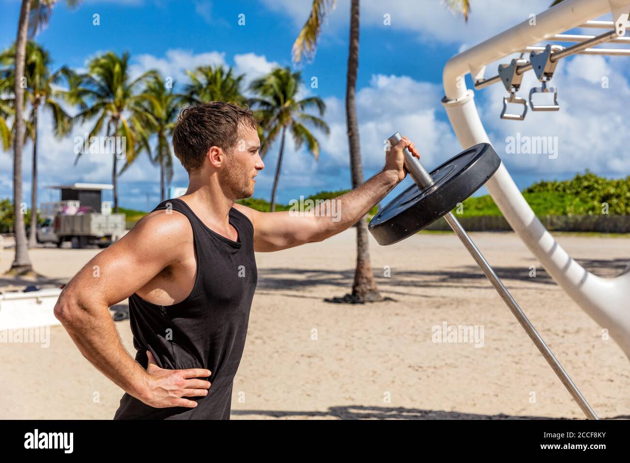 Outdoor Gym - Fitness man working out biceps muscles at outdoor public calisthenic gym on South Beach doing T-bar barbell extensions training on South Stock Photo