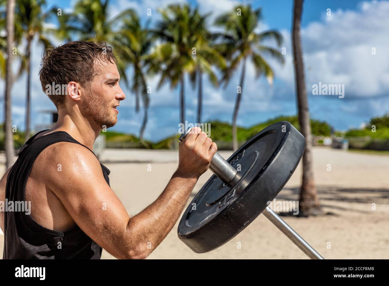 Outdoor calisthenics gym park male athlete working out on T-bar outside in summer. Man workout strength training arms biceps muscles with heavy Stock Photo