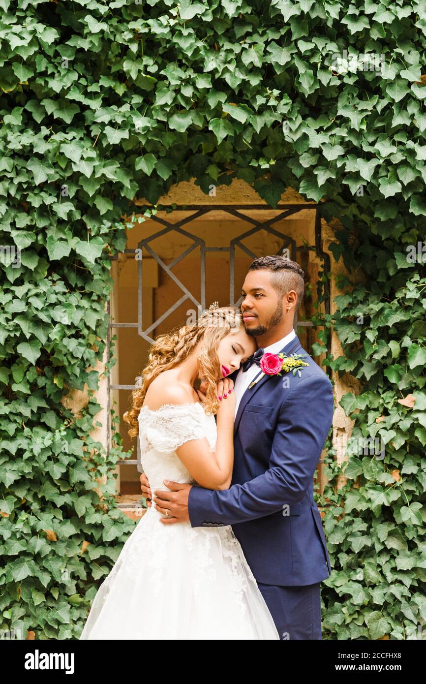 Wedding, newlyweds, young adults, diversity, portrait garden, window, hug Stock Photo