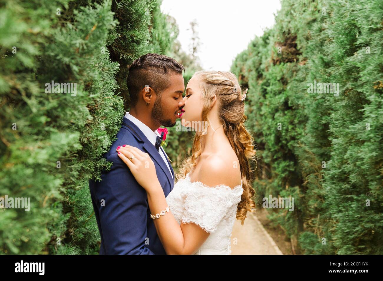 Wedding, newlyweds, young adults, diversity, love, garden, hedge, kissing Stock Photo