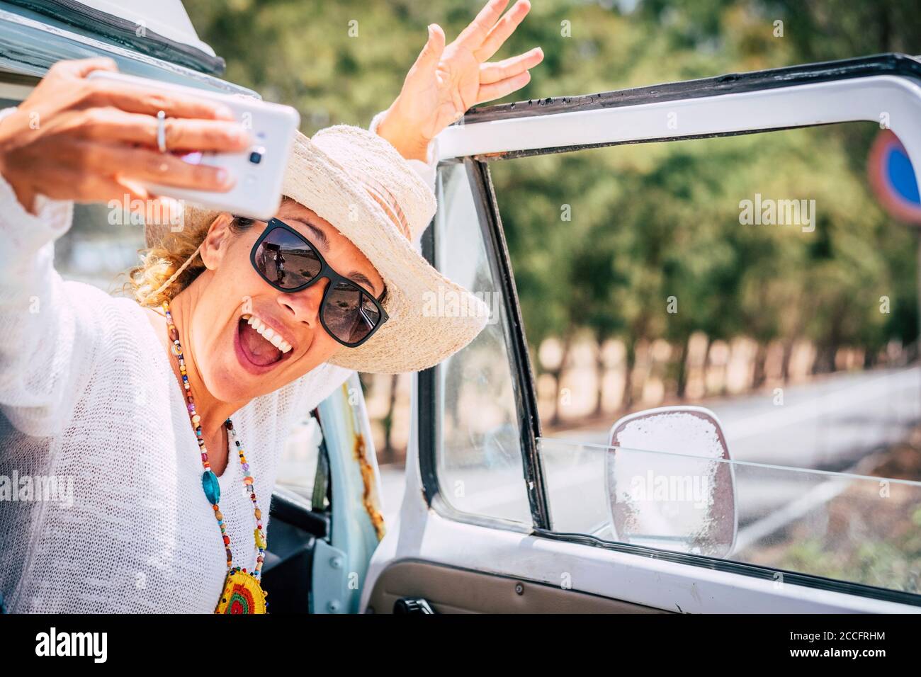Happy and cheerful young beautiful caucasian lady take selfie picture outside her retro van vehicle enjoying the trip and travel lifestyle - summer ho Stock Photo