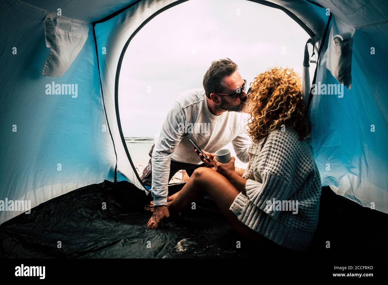 Travel couple people with camping activity kissing and having relax together - two adult with tent camp enjoy holiday vacation in total freedom Stock Photo