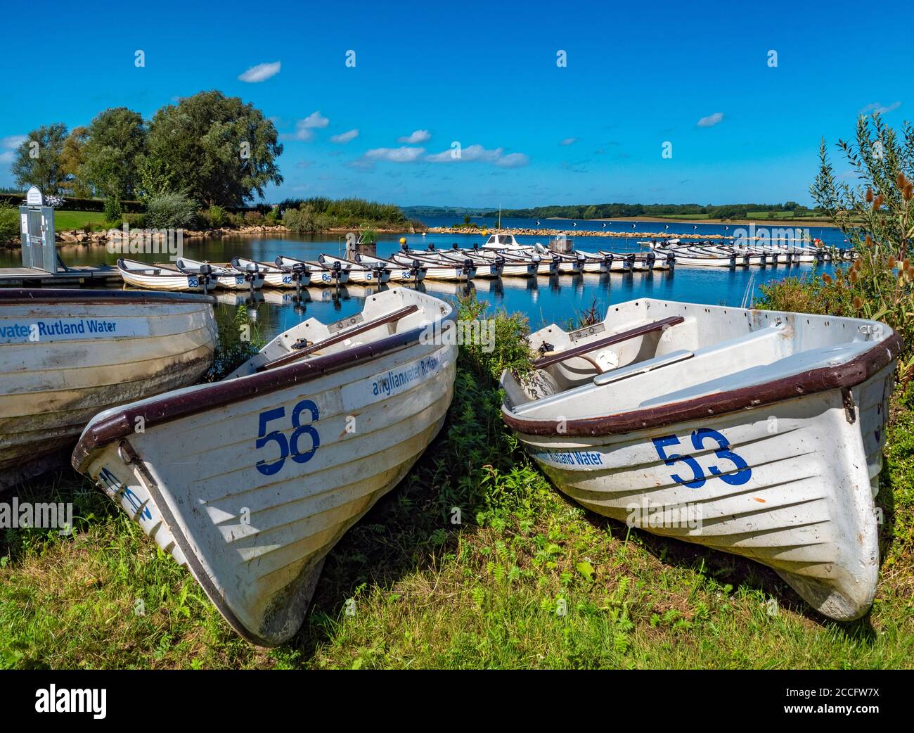 Numbered boats on land, with a line of motor boats behind on Rutland Water – a reservoir, artificial lake and nature reserve in Rutland, England, UK. Stock Photo