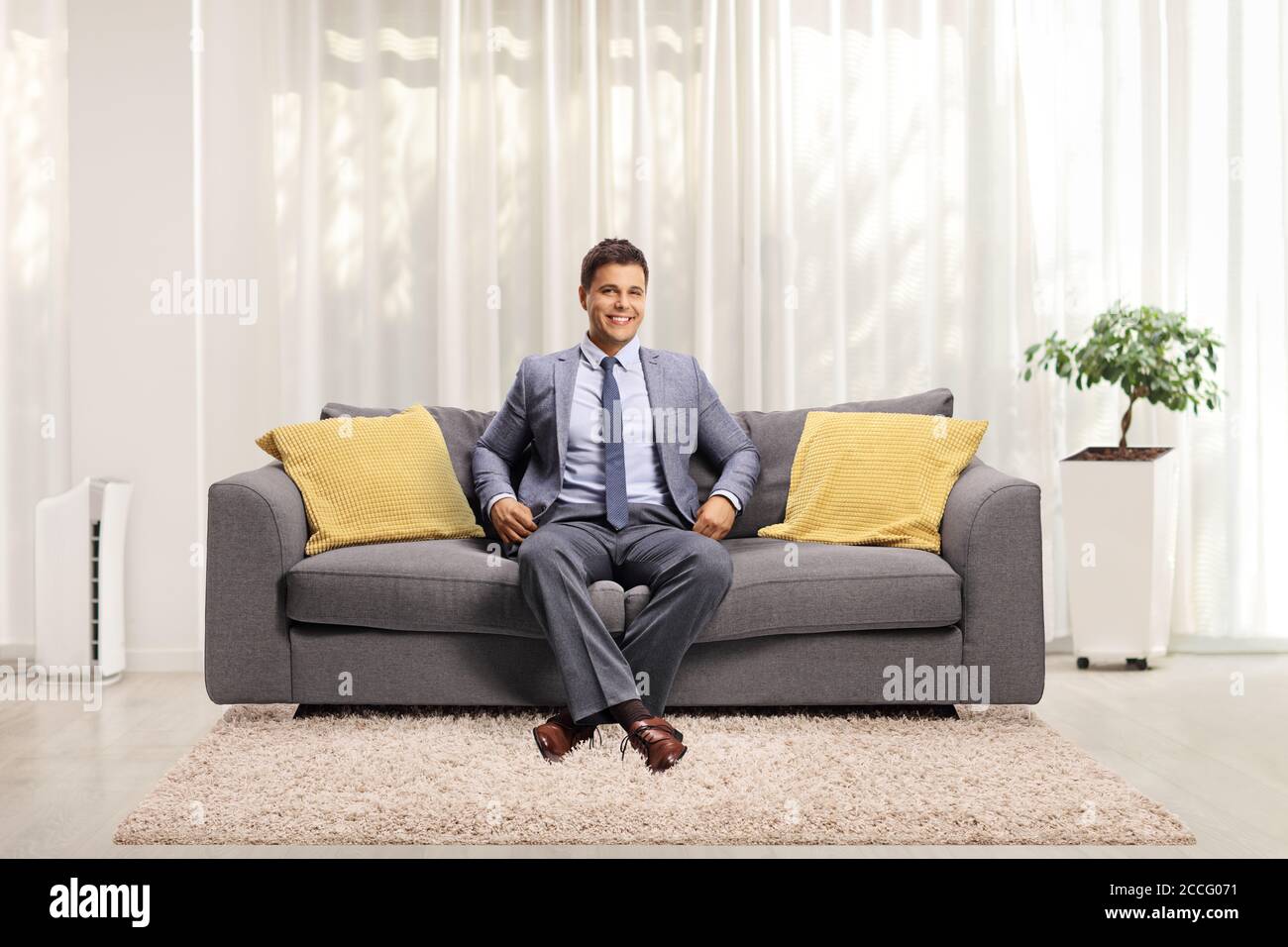 Professional young man sitting on a gray sofa at home and smiling at the camera Stock Photo
